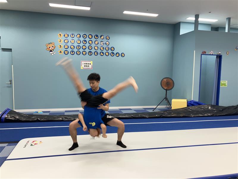 側宙をする子どもとサポートする体操教室の先生の様子