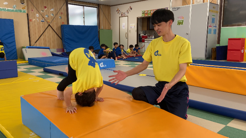 体操教室で補助されながら前転をする男の子の様子