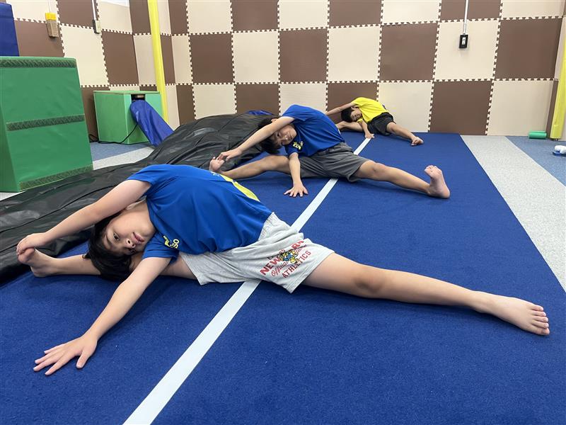 開脚をして体を右に倒しストレッチをする子どもたちの様子