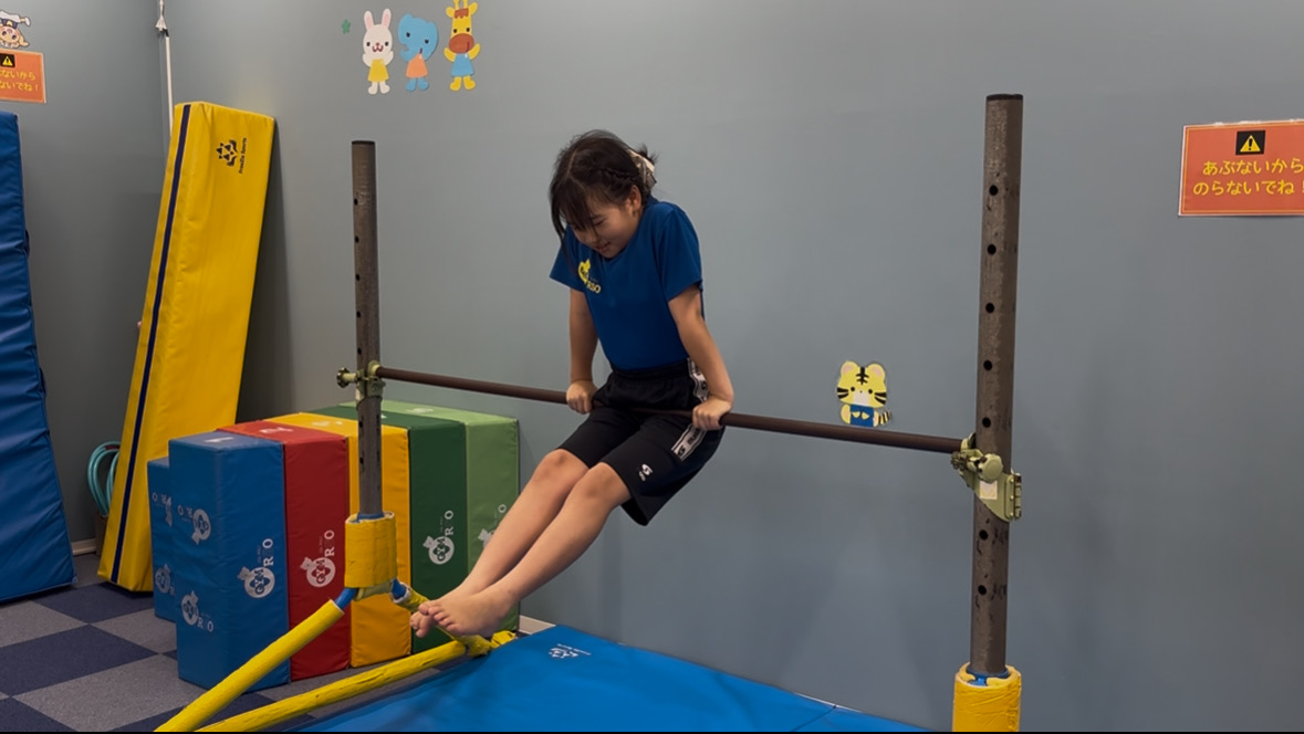 鉄棒で空中前回りを回るための勢いをつける子ども