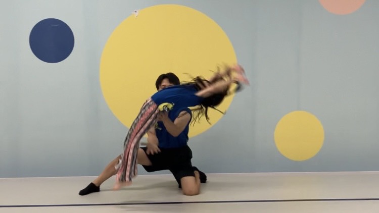 マットの上でロンダート宙返りをする女の子と補助をするインストラクターの様子