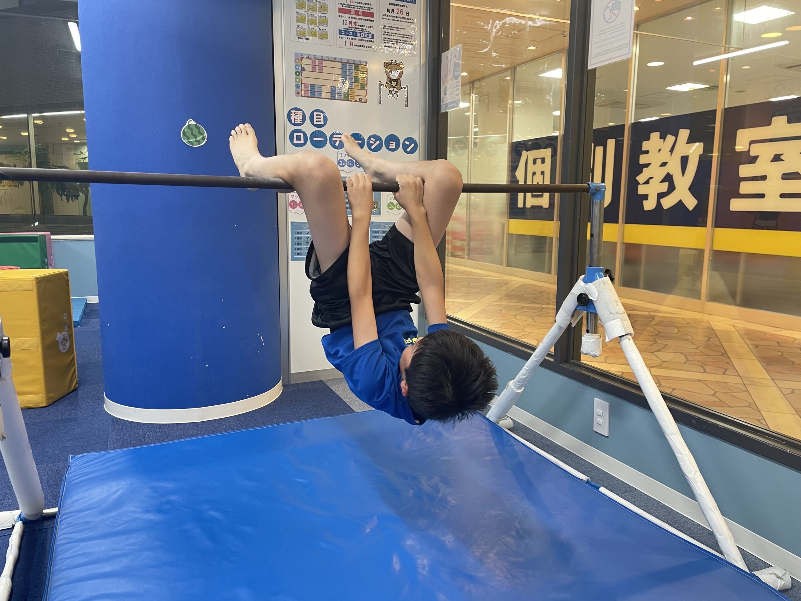 鉄棒に腕でつかまりながら足をかけて逆さの状態になっている男の子の様子