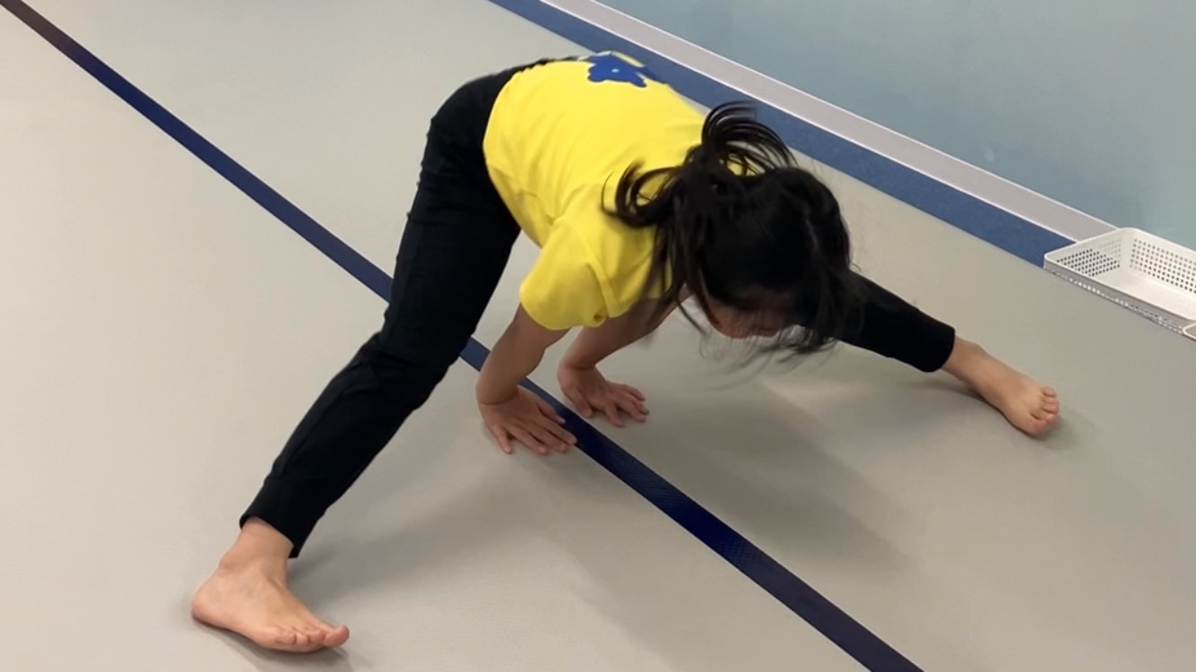 開脚前転での回転後に地面を手で押し立ち上がりの練習をしている女の子の様子