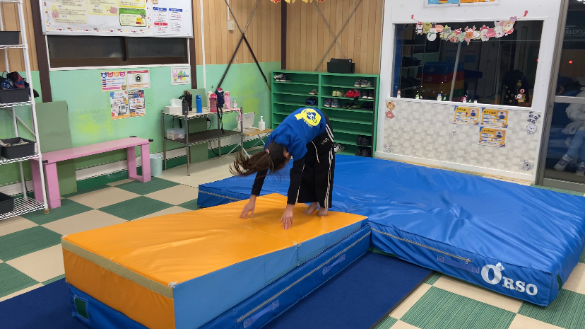 傾斜ブロックの上で前屈の姿勢を取り、坂の下がる向きで伸膝後転を行う前の様子