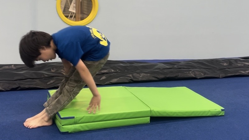 回転する方向に傾斜のあるマットを置き伸膝後転の練習をする男の子の様子