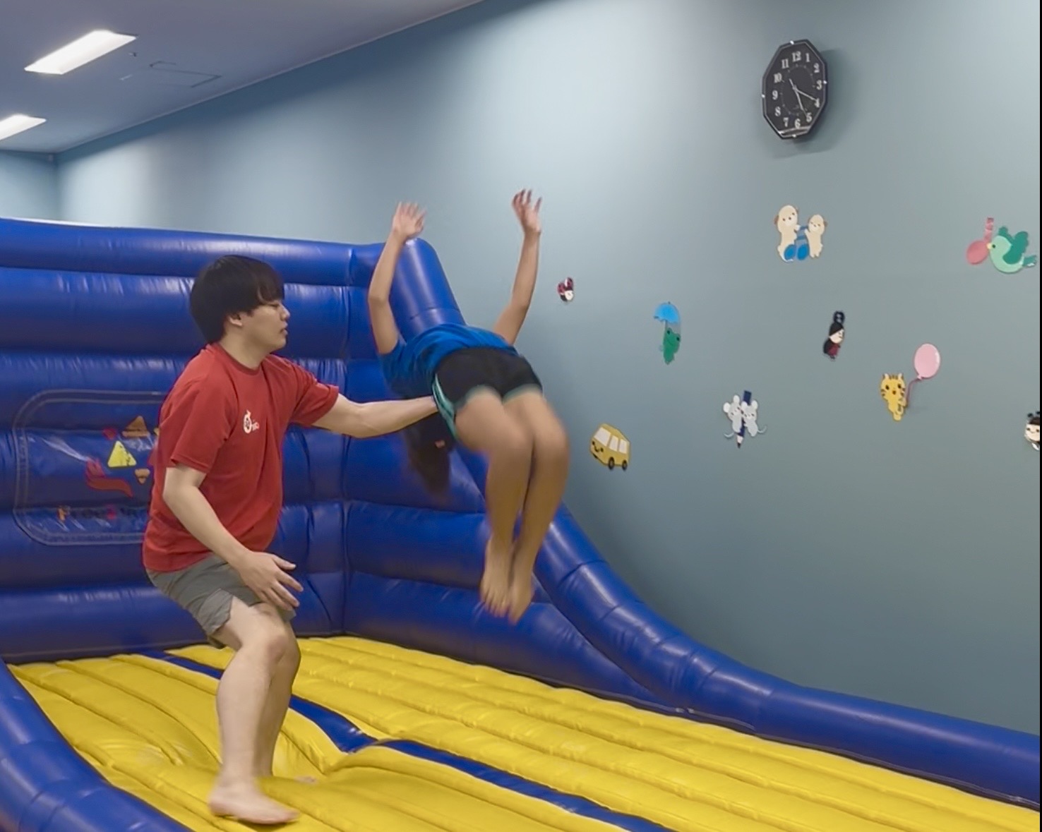 トランポリンの上で宙返りをする子どもと背中をサポートする先生の様子