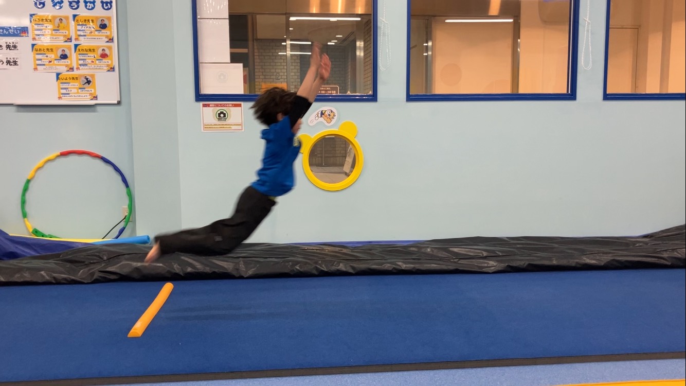 上に向かって大きく腕を振りながら、前方にジャンプしている立ち幅跳びの踏切の様子