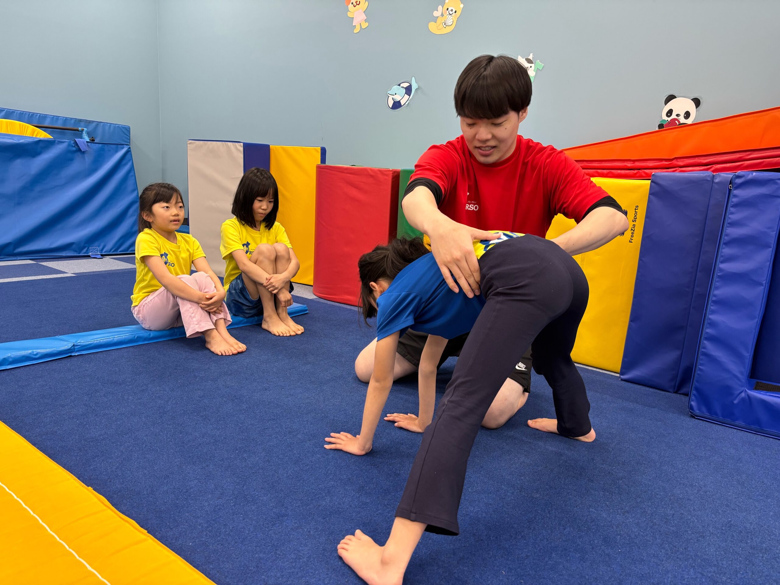 両足を大きく開き手を床について開脚前転の練習をする様子