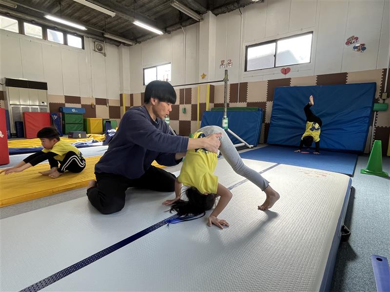 両足を大きく開き手と頭を床について開脚後転の練習をする様子